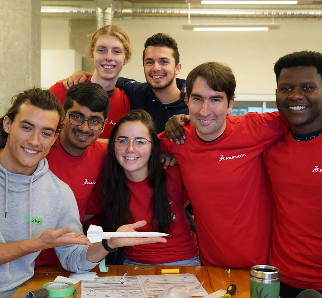 Estudantes com camisetas SOLIDWORKS apresentando um projeto de foguete