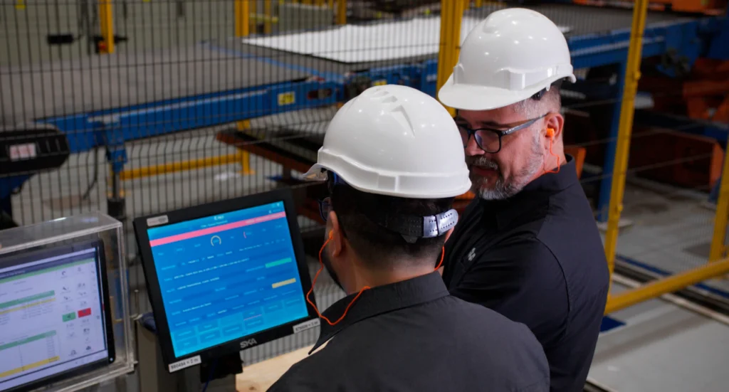 Trabalhadores de capacete branco olhando tela do Syneco na indústria